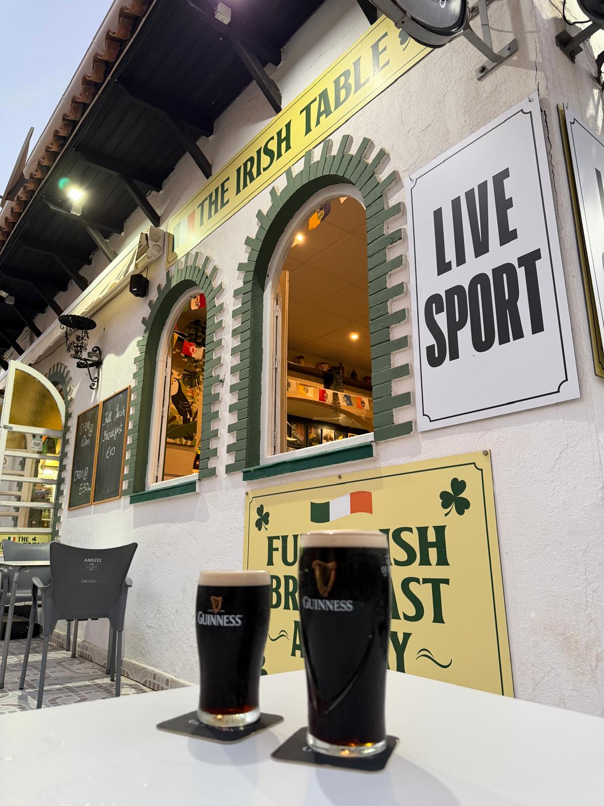 Two pints of Guinness outside The Irish Table beside the Live Sport sign